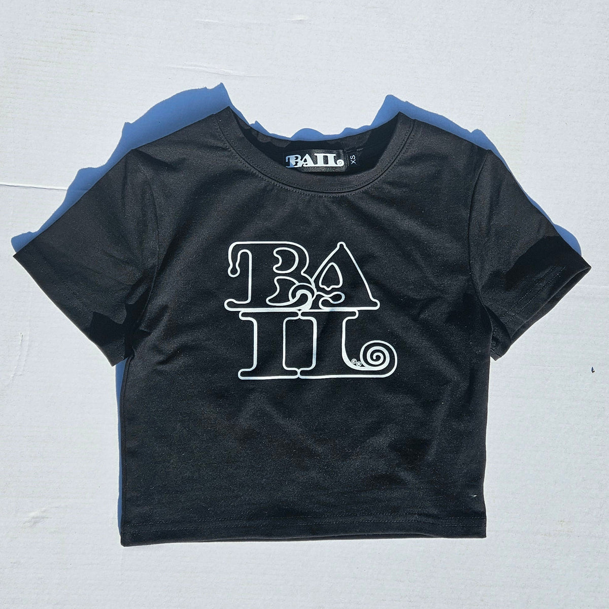A black short-sleeve crop top t-shirt with a white graphic print reading 'BAIL' on the front, laid flat on a white background.