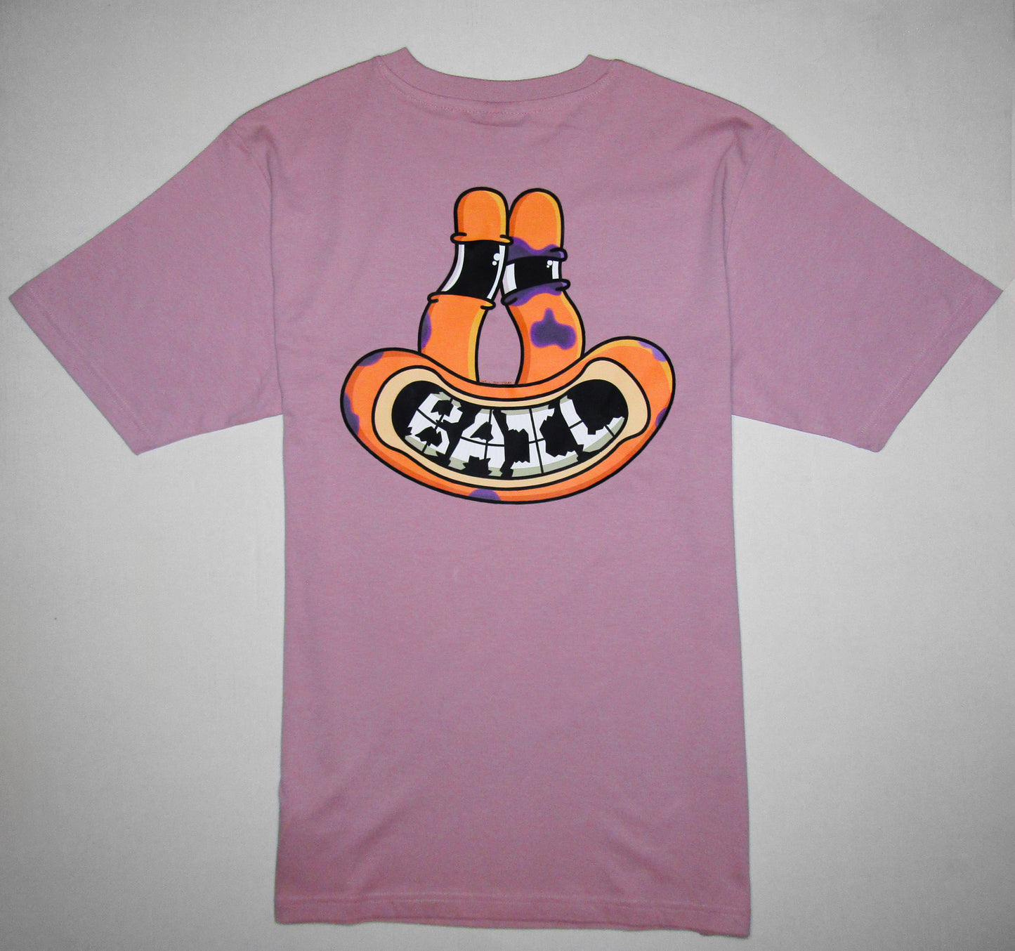The back of a light pink T-shirt with a bold, playful graphic on the back, featuring a smiling orange cartoon frog with the word "BAIL" in stylised letters as teeth. The cartoon has long, slightly squinted eyes, purple bruises scattering the face and one black eye, evoking a casual vibe.