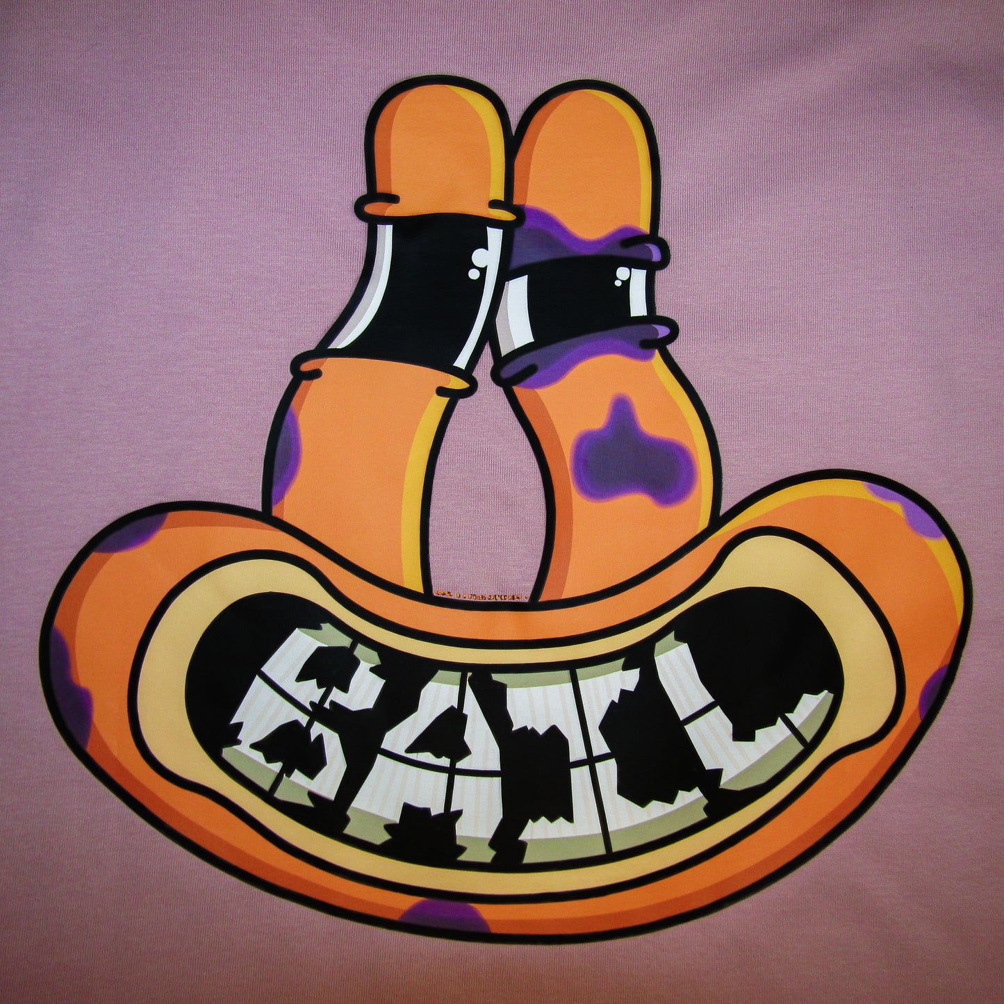 Colourful cartoon art on the back of a pink 100% cotton tee featuring an orange alien frog face with tall eyes and a wide, black-and-white grinning mouth with cracked teeth spelling the clothing brand's name,  "BAIL." The face has purple bruises and a black eye, indicating the frog fell while skateboarding, yet it has a happy, relaxed expression.
