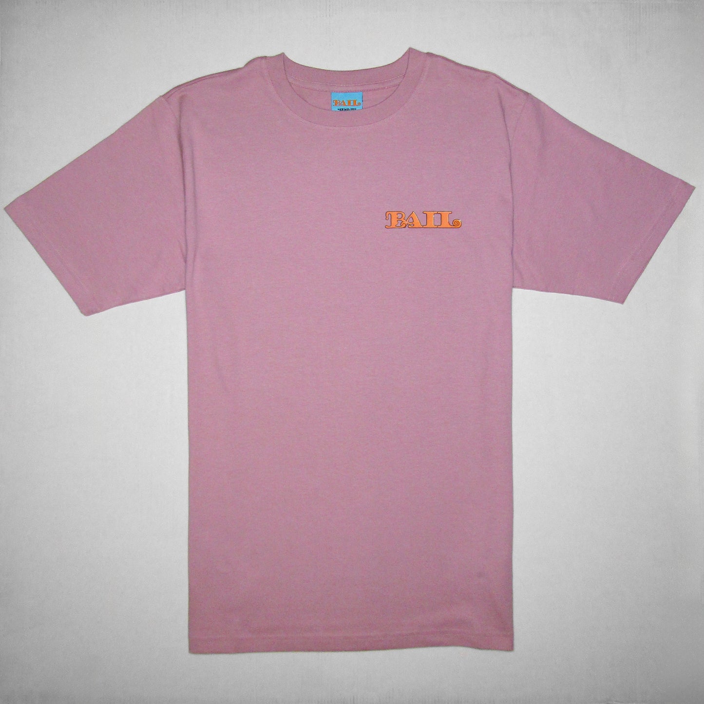 A light pink crew-necked T-shirt with short sleeves is displayed flat against a white background. The clothing brand's logo, "BAIL" in bold orange font, is printed in orange on the left chest.